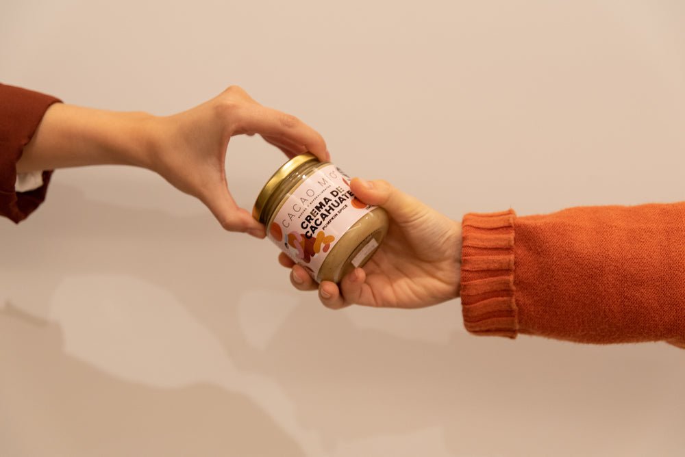 Crema de Cacahuate Pumpkin Spice - imagen dos manos y frasco de crema de maní sabor pumpkin spice